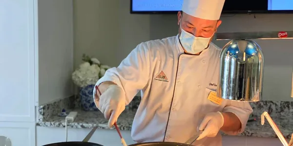 A chef in white uniform and mask preparing food.